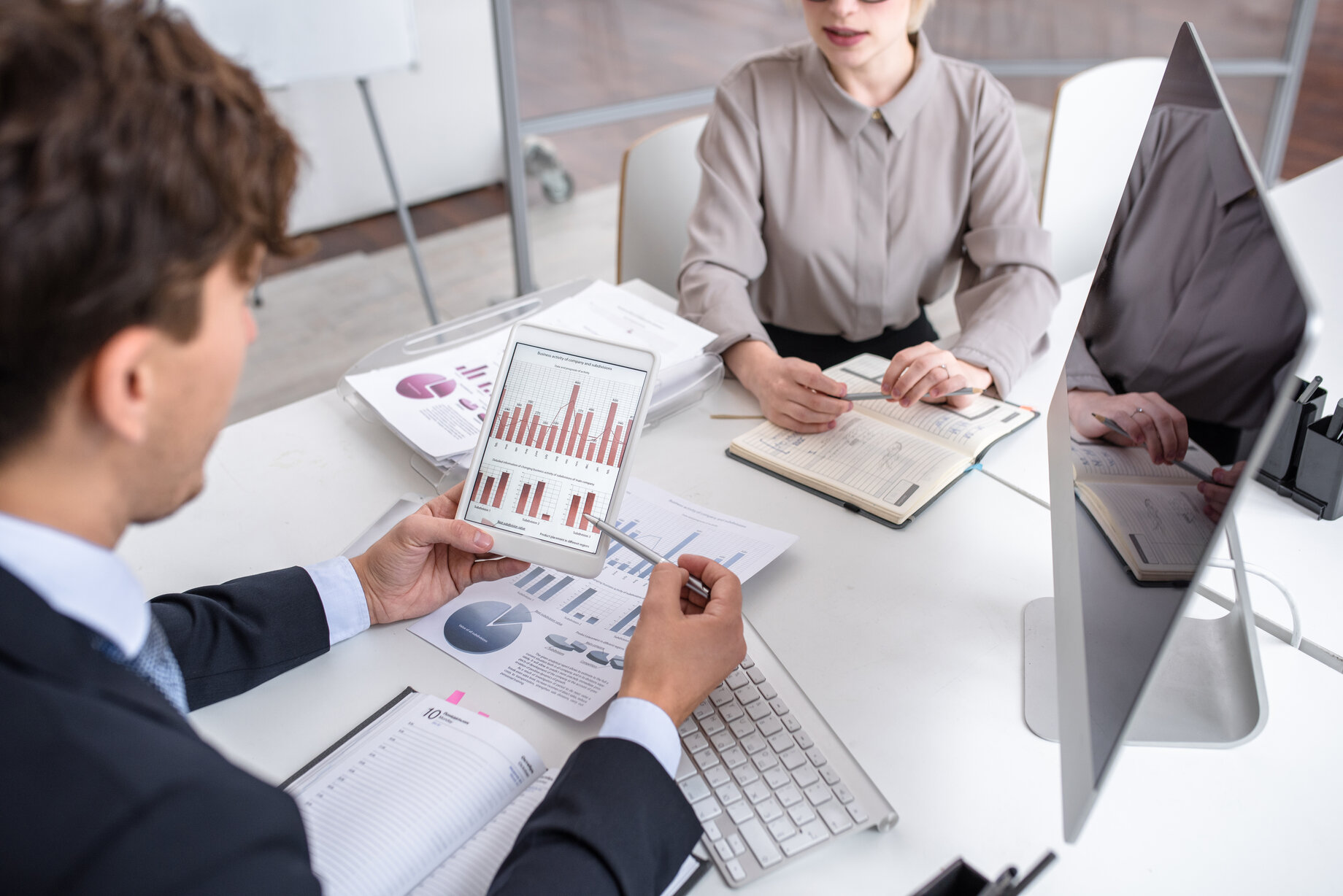 A man and woman sitting at a desk looking at graphs on a tablet.