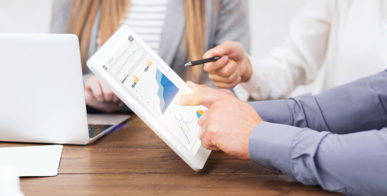 A group of people sitting at a table with a tablet displaying graphs.