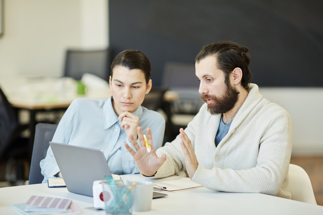 Two people sitting at a table looking at a laptop.