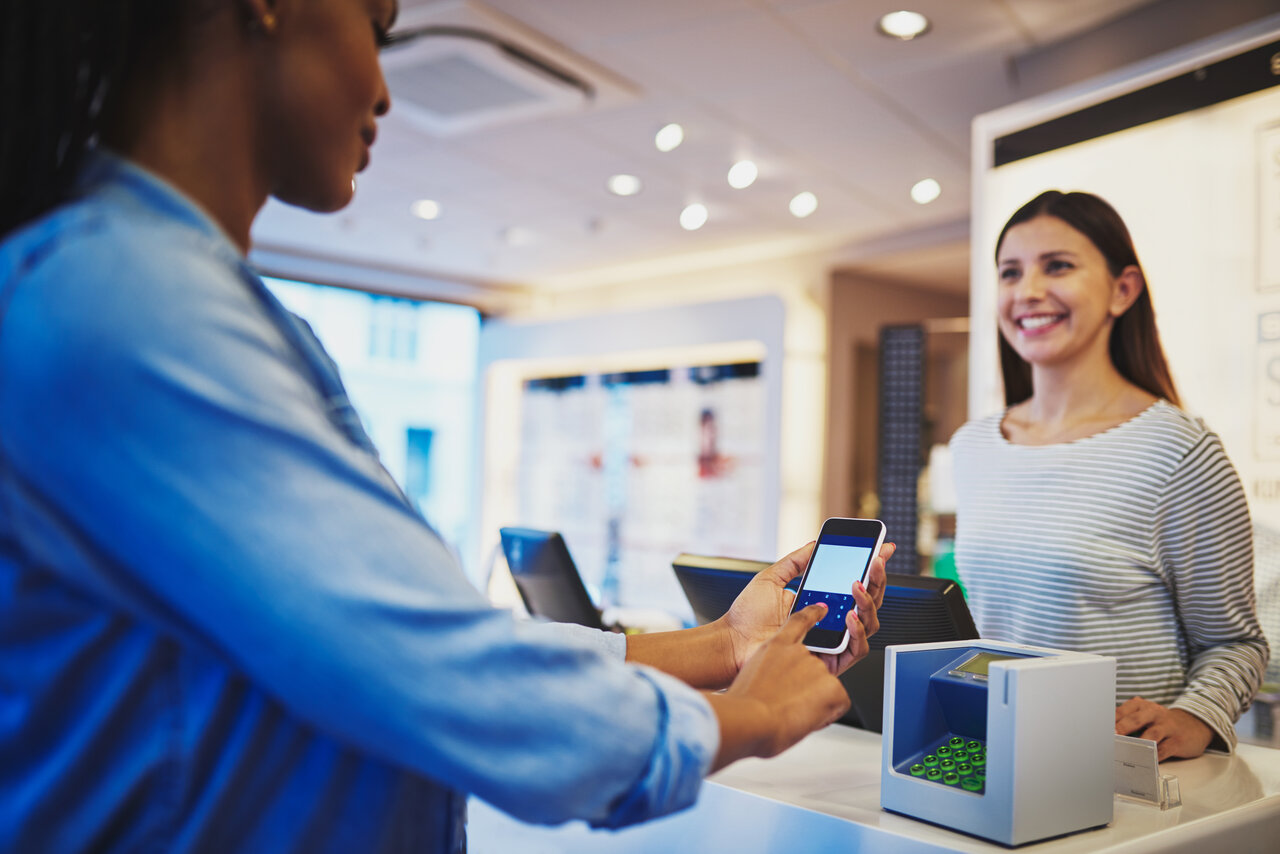 A woman is handing over her phone to a woman at a store.