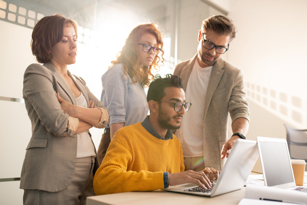 Group of pensive creative advertisers standing at desk and asking web designer to add design elements for presentation in office for WordPress hosting